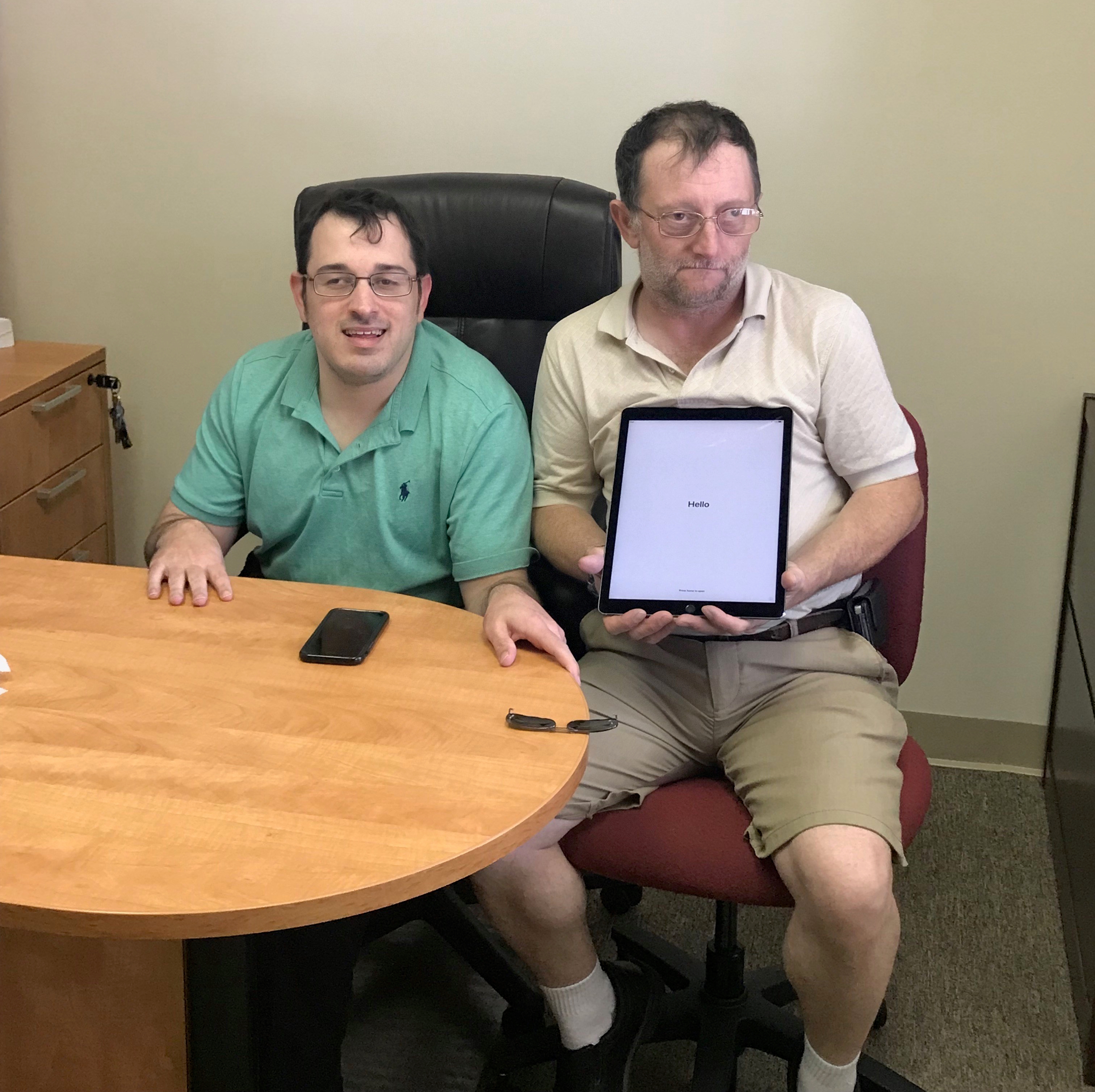 Matt Shelor, smiling, seated at desk beside consumer holding an iPad Pro